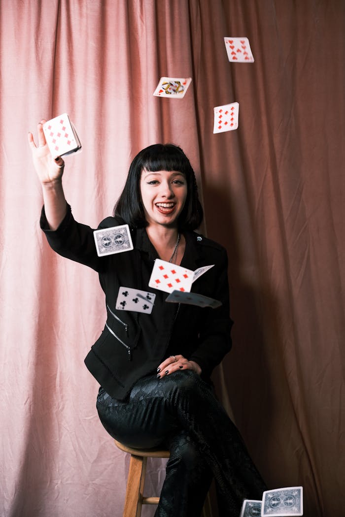 A young woman performs a card trick indoors, showcasing her magic skills with flair and style.