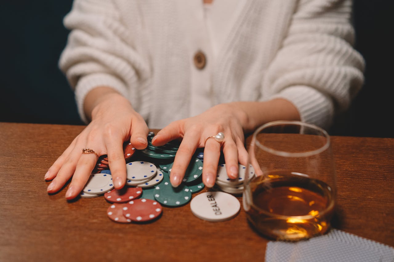 Hand playing poker with chips on a wooden table, paired with whiskey.