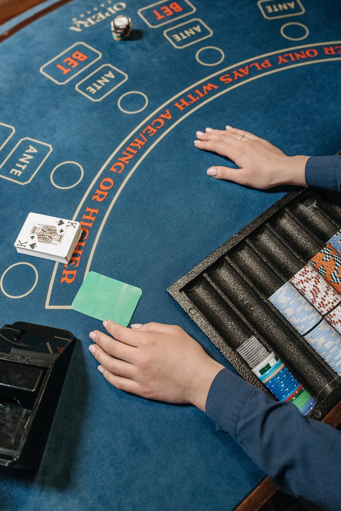 Casino table with dealer's hands, cards, and chips in a gambling setting.